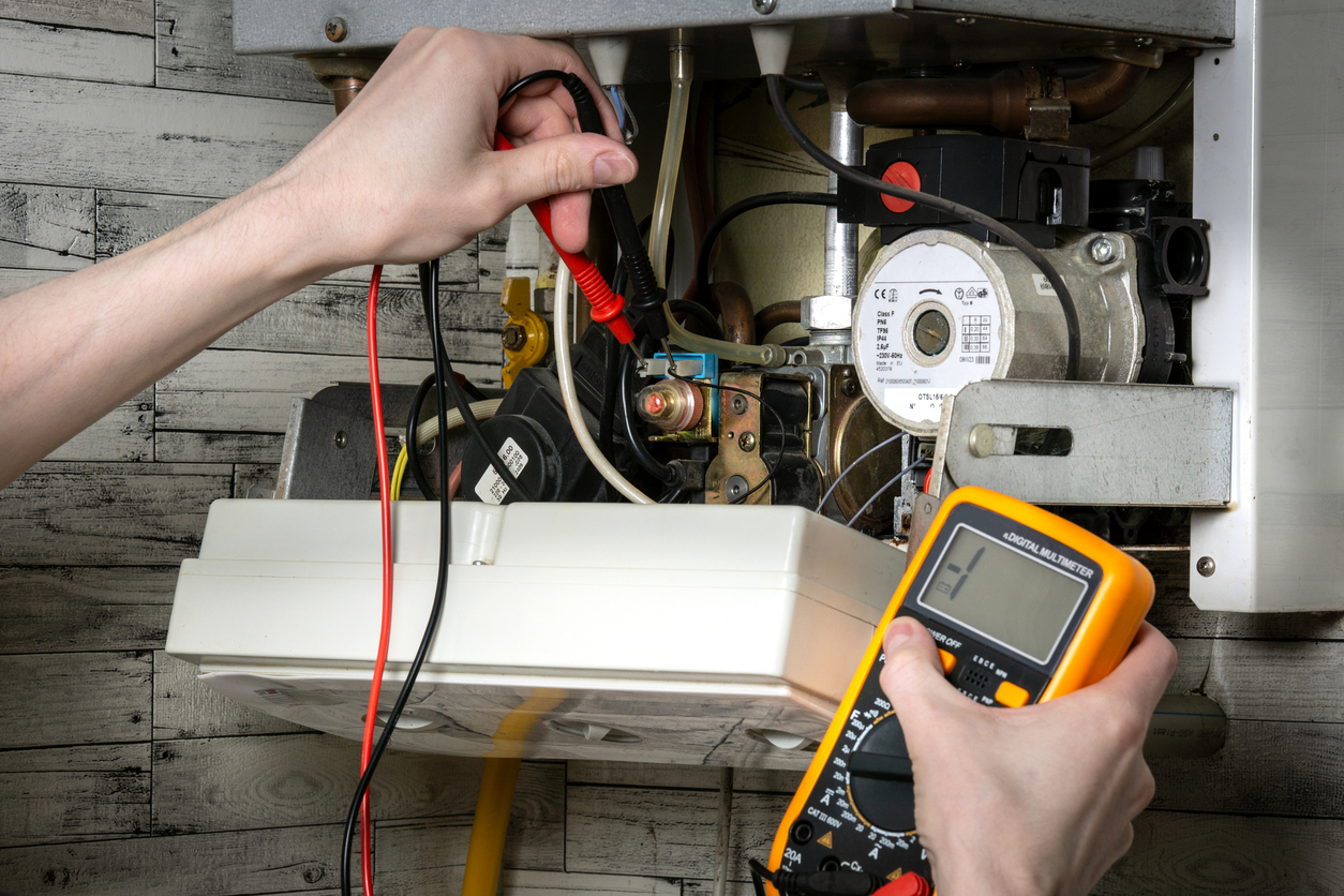 Close-up of multimeter probes checking electrical components in an open water heater.