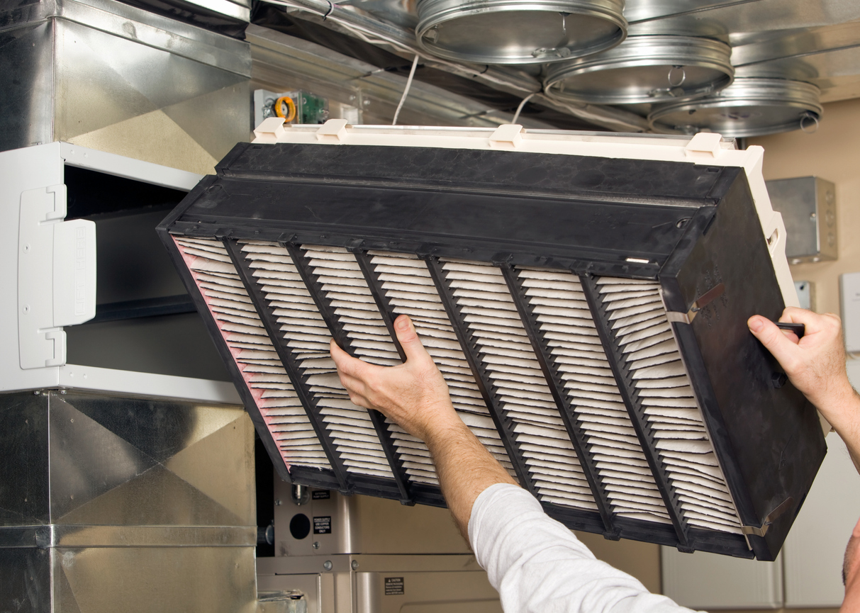A technician replacing a whole house air purification filter in a ventilation system.